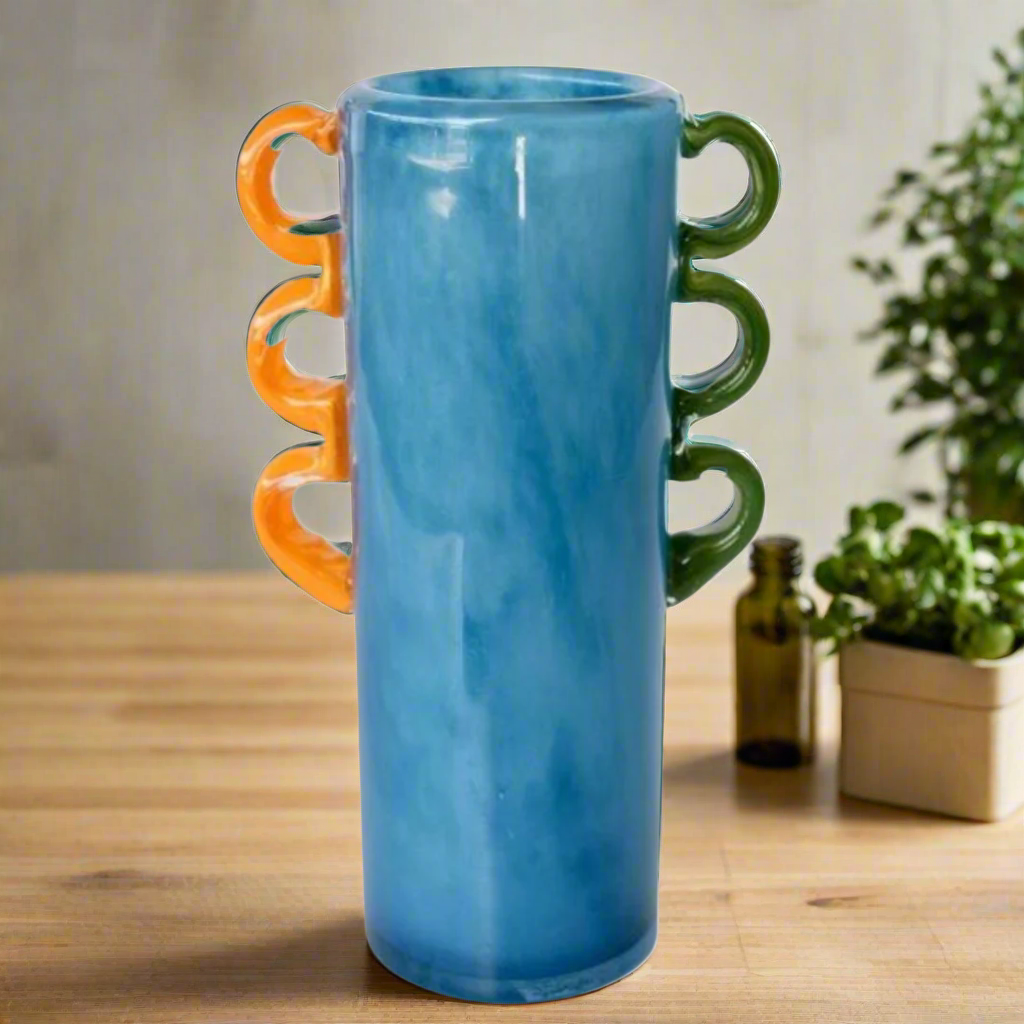 Tall Blue Glass Vase: A Stunning Decorative Piece
Add a pop of color and elegance to your home with our expertly crafted Tall Blue Glass Vase. Featuring vibrant orange and green handles, this unique piece is sure to elevate your interior design. Unique Boys.