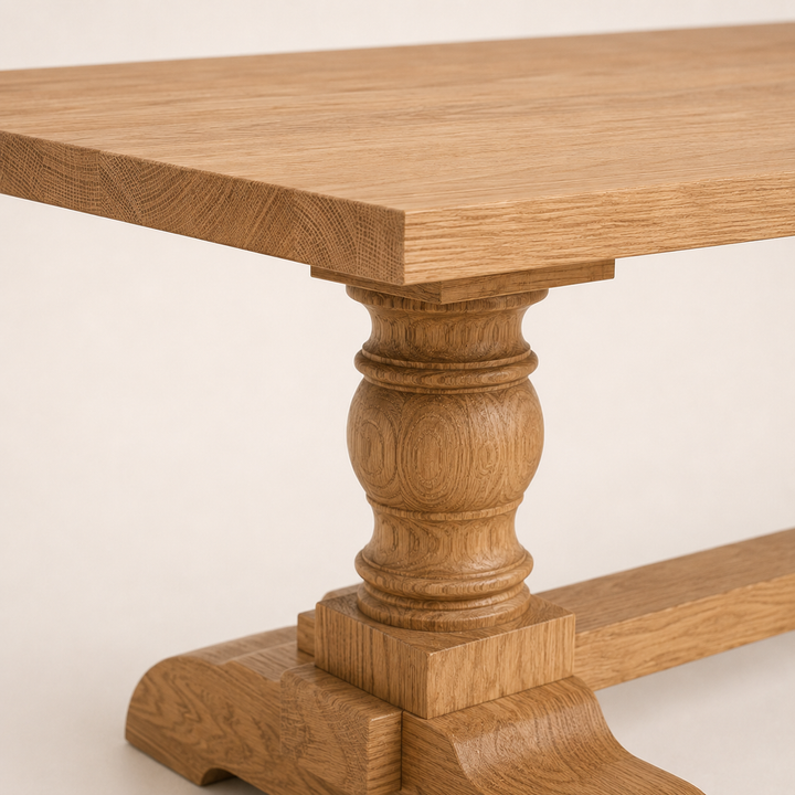 Close-up of a wooden dining table showing the tabletop, turned pedestal leg, and stretcher base in a warm oak finish against a light neutral background.