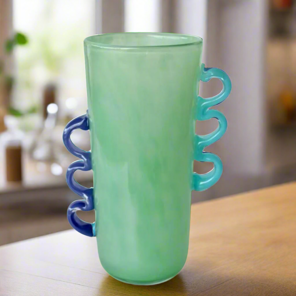 Tall Green Glass Vase with Purple &amp; Blue Handles
Elevate your home decor with this stunning Tall Green Glass Vase, featuring vibrant purple and blue handles. Its unique design and beautiful green hue make it perfect for displaying flowers or as a standalone decorative piece.Unique Boys.