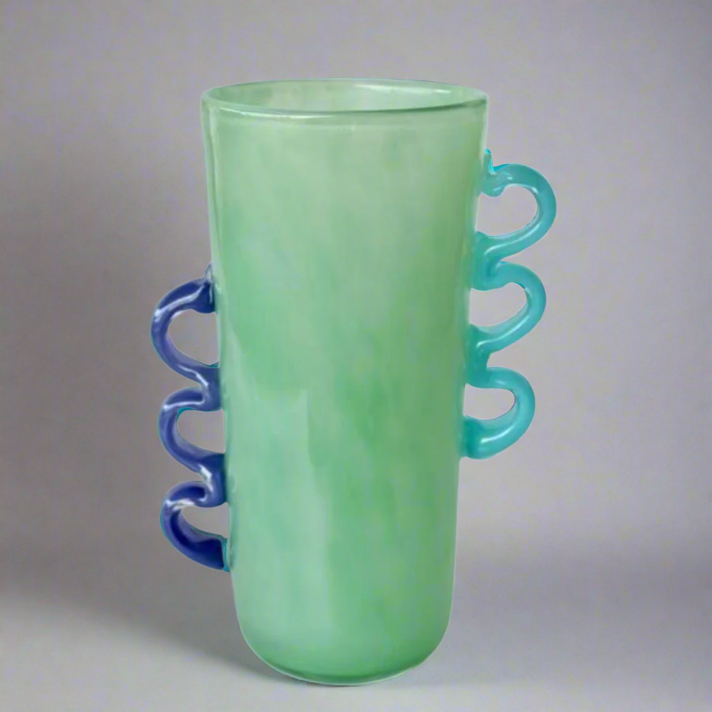Tall Green Glass Vase with Purple &amp; Blue Handles
Elevate your home decor with this stunning Tall Green Glass Vase, featuring vibrant purple and blue handles. Its unique design and beautiful green hue make it perfect for displaying flowers or as a standalone decorative piece.Unique Boys.